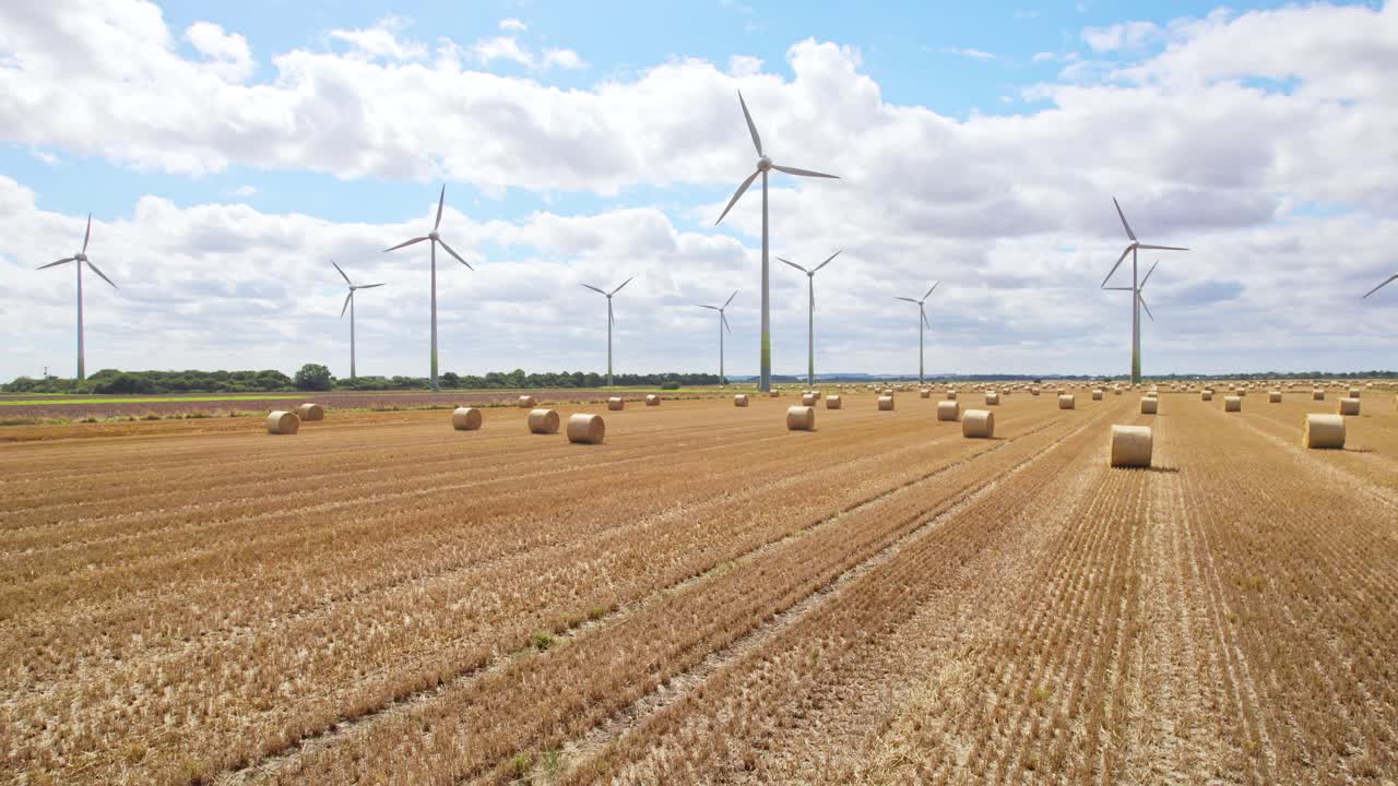 High above, the camera records the tranquil scene of wind turbines spinning gracefully in a Lincolnshire farmer's field, recently harvested and adorned with golden hay bales