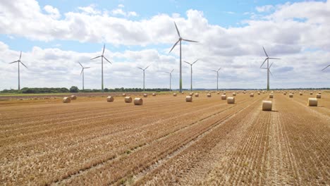 high above, the camera records the tranquil scene of wind turbines spinning gracefully in a lincolnshire farmer's field, recently harvested and adorned with golden hay bales