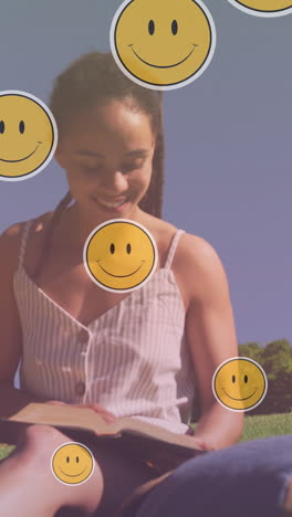 animación de iconos emoji sobre una mujer biracial sonriente leyendo en el parque