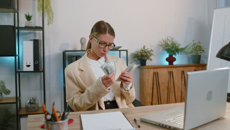 Business-woman-counting-money-cash-income-earnings,-calculate-financial-bills-use-laptop-at-office