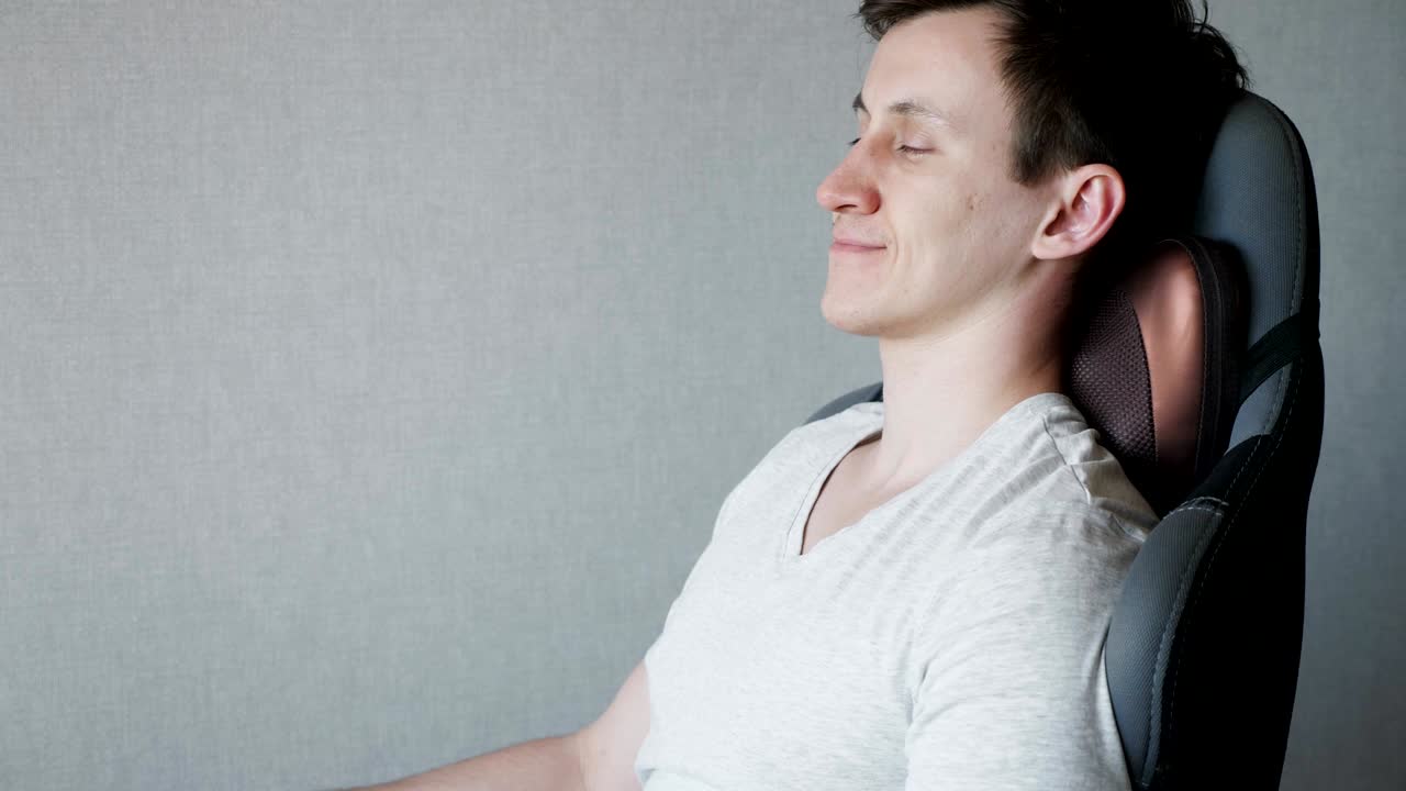 젊은 남자는 전기 마사지 베개와 함께 의자에 앉아 있습니다