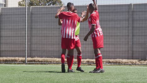 Animation-of-social-media-icons-over-team-of-diverse-male-soccer-players-celebrating-on-sports-field