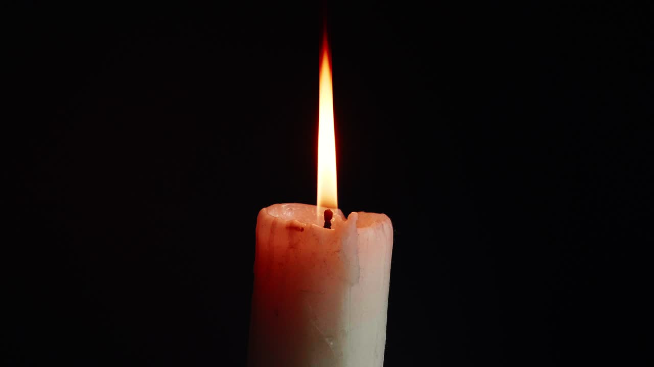 Přehlídka barevných jednotlivých svíček na černém pozadí s efektem světla a zpomaleného pohybu.