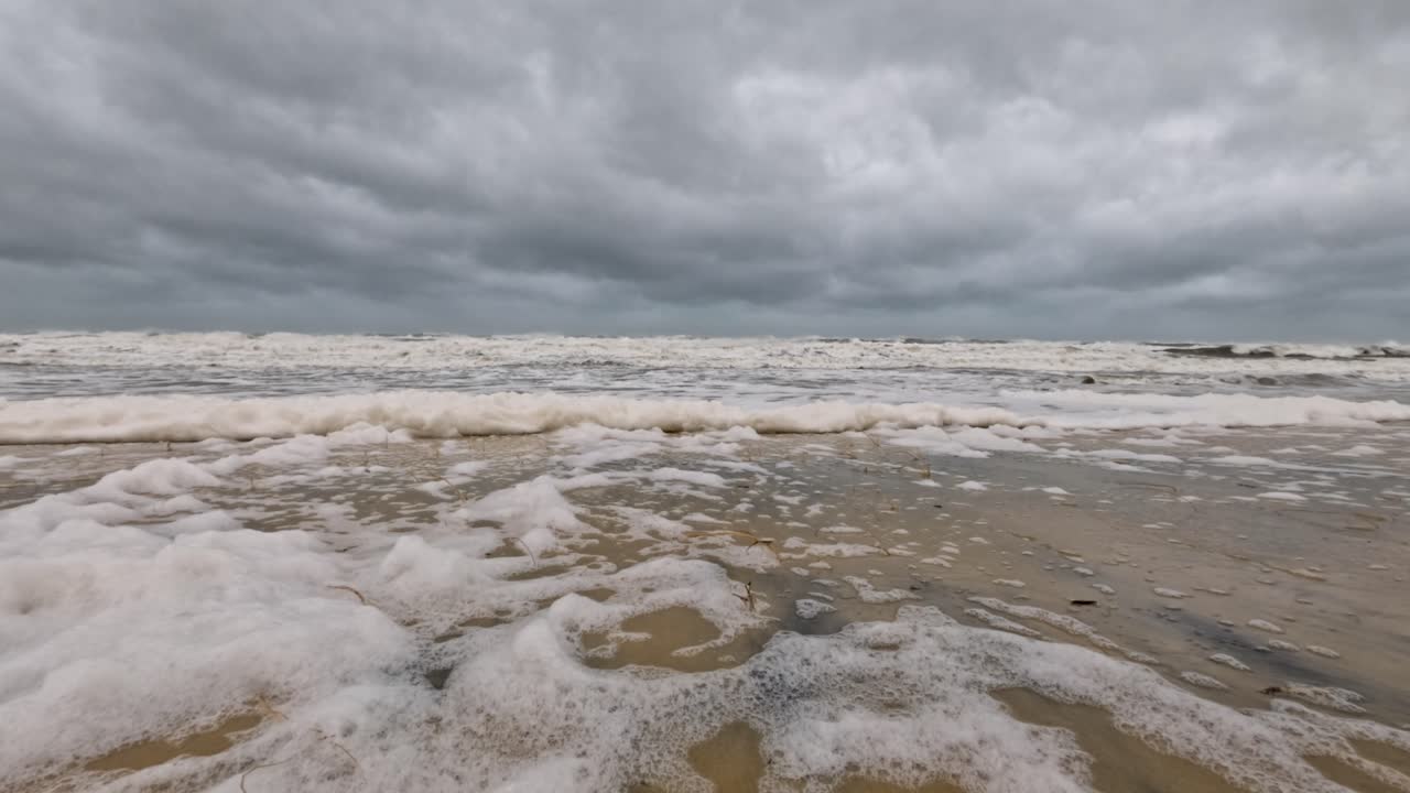 파도가 해변에 부히며 폭풍우 하늘 아래에서 거품을 만들어, 다가오는 사이클론의 힘과 분위기를 포착합니다.