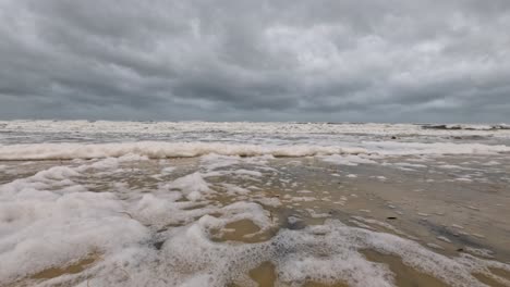 waves crash onto a beach, creating foam under stormy skies, capturing the power and mood of an approaching cyclone