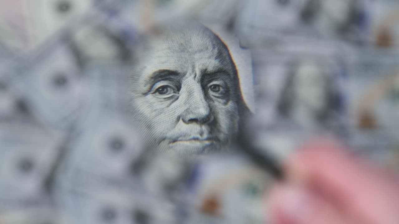 un lote de billetes de cien dólares inspeccionando bajo una lupa