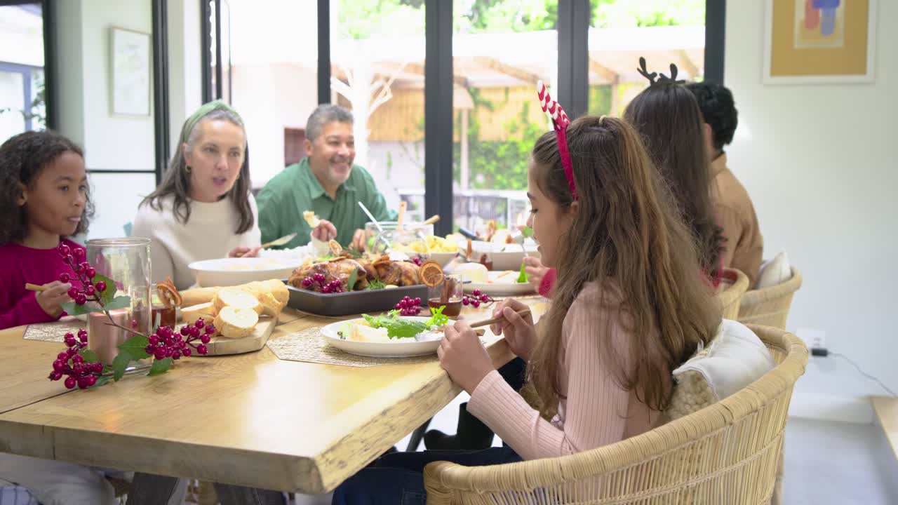 Diverse family at table passing turkey following woman's toast, girl smiling at camera