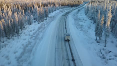 Aerial,-drone-shot,-overlooking-a-truck,-driving-on-arctic-road,-surrounded-by-snowy-sitka-forest,-winter-sunset,-in-Gakona,-Alaska,-USA