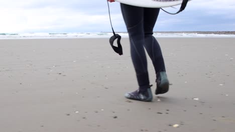 pies de hombre caminando hacia el océano con una tabla de surf y traje de neopreno listo para surfear