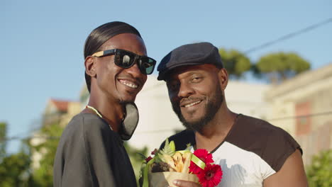 portrait of happy gays with bouquet of flowers looking at camera