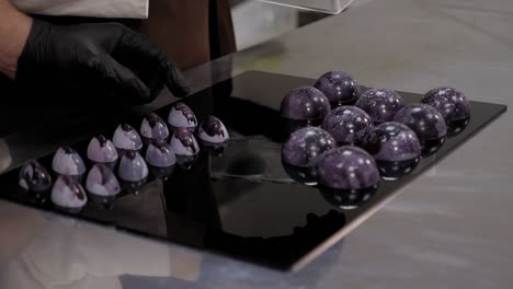primer plano de un chef de pastelería colocando chocolates de colores en una superficie de espejo negro.