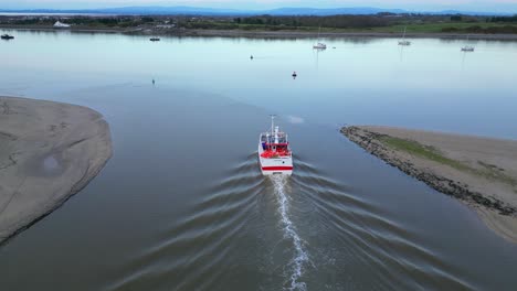 un arrastrero de pesca que sale del afluente de marina y entra en aguas tranquilas en el estuario del río wyre fleetwood lancashire reino unido al anochecer