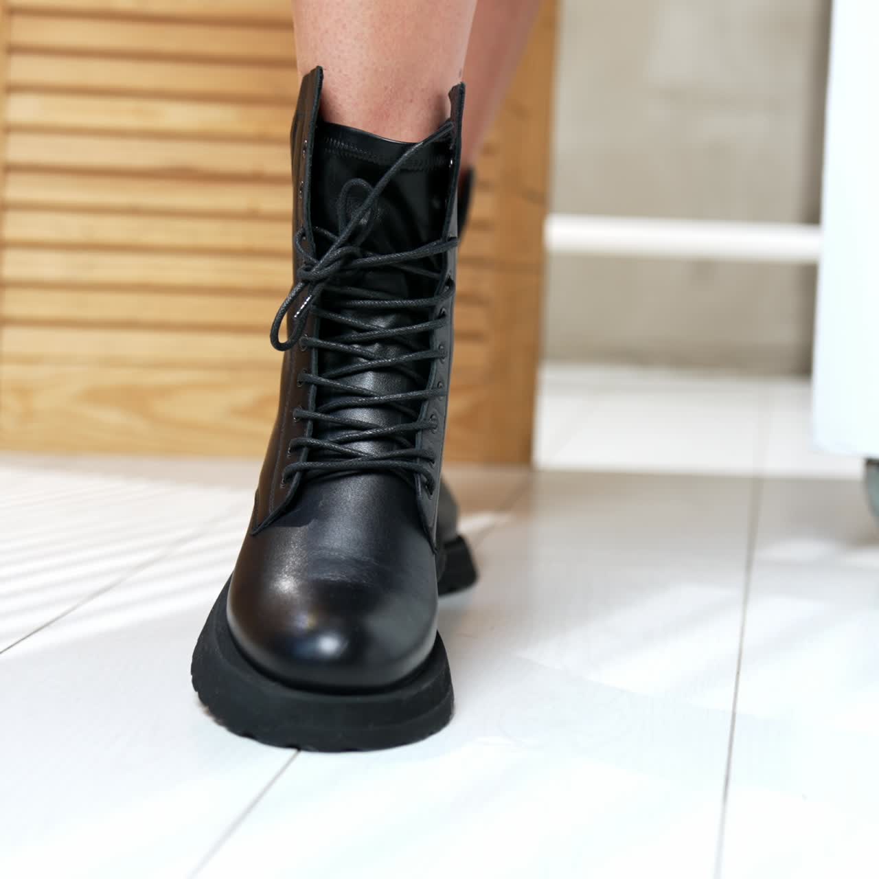 Demonstration of stylish army boots with laces on female feet. Woman moving her feet in fashionable footwear in front of camera. Close up. Wooden screen at backdrop