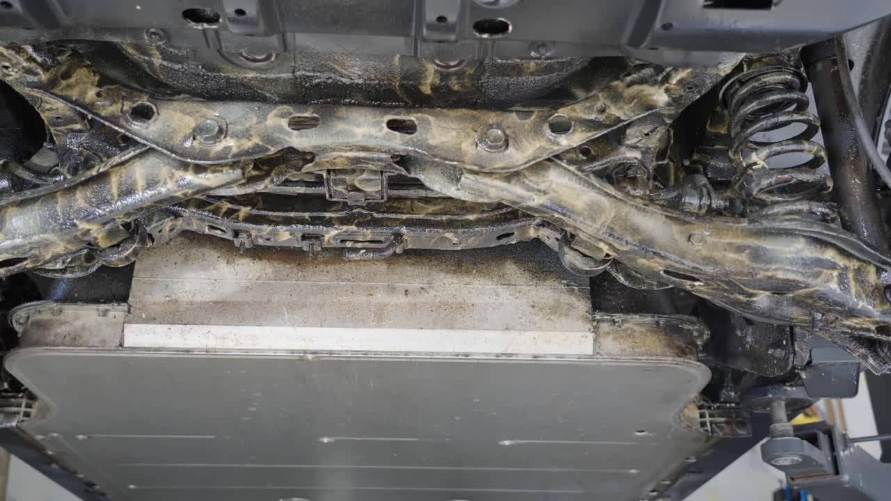 Slow right to left tracking shot showing results after applying lanolin rust protection to underside of electric vehicle