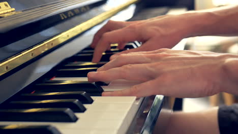 un primer plano de un hombre tocando un piano negro con las manos y los dedos a la luz de una ventana