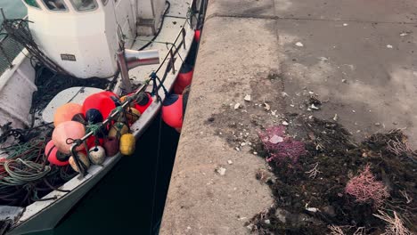 un barco de pesca amarrado a muelles de hormigón, adornado con boyas de colores, encarnando la esencia marítima de una pequeña ciudad de pescadores