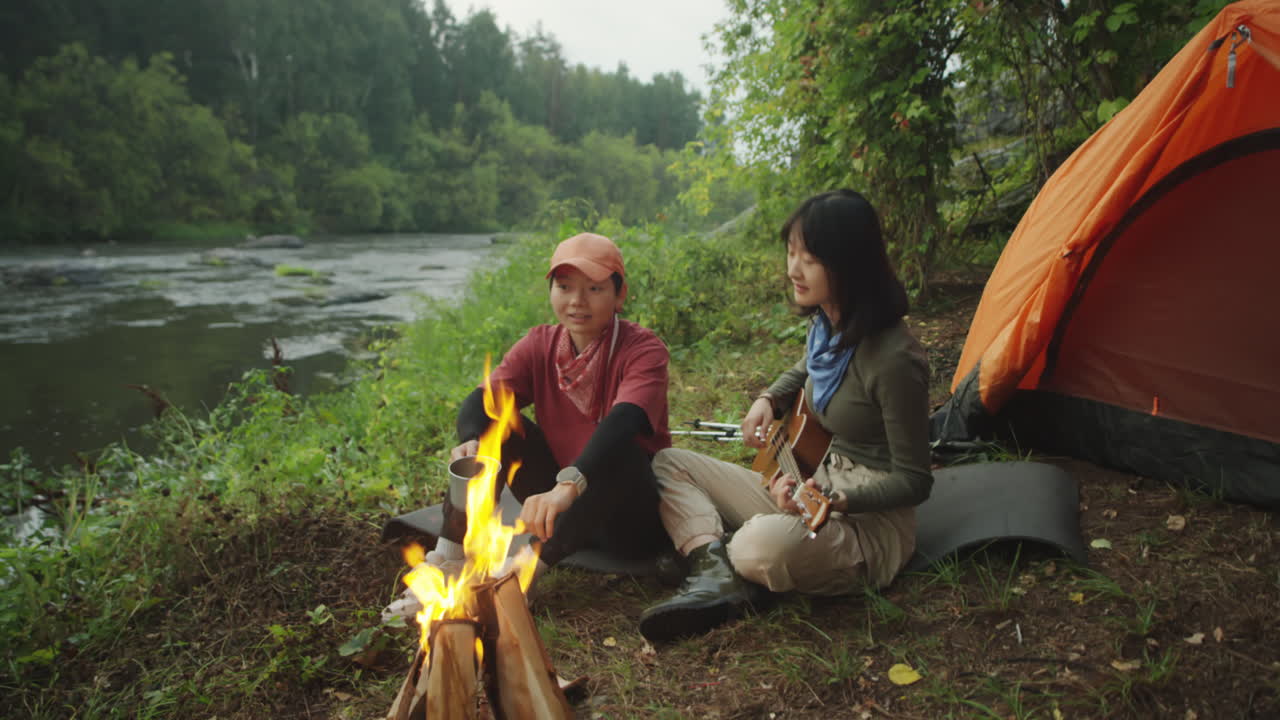 Female Tourists Playing Guitar by Campfire