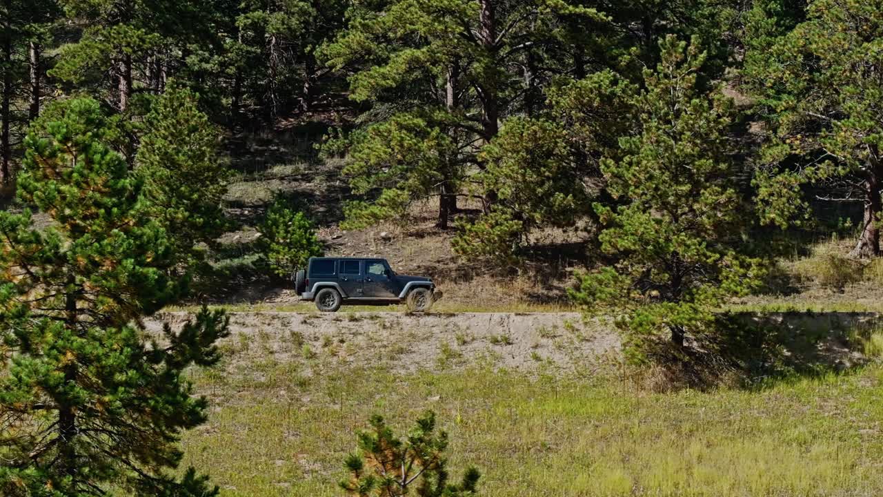 Drone view of a vehicle driving through a forest on a dirt trail, with sunlight filtering through the trees
