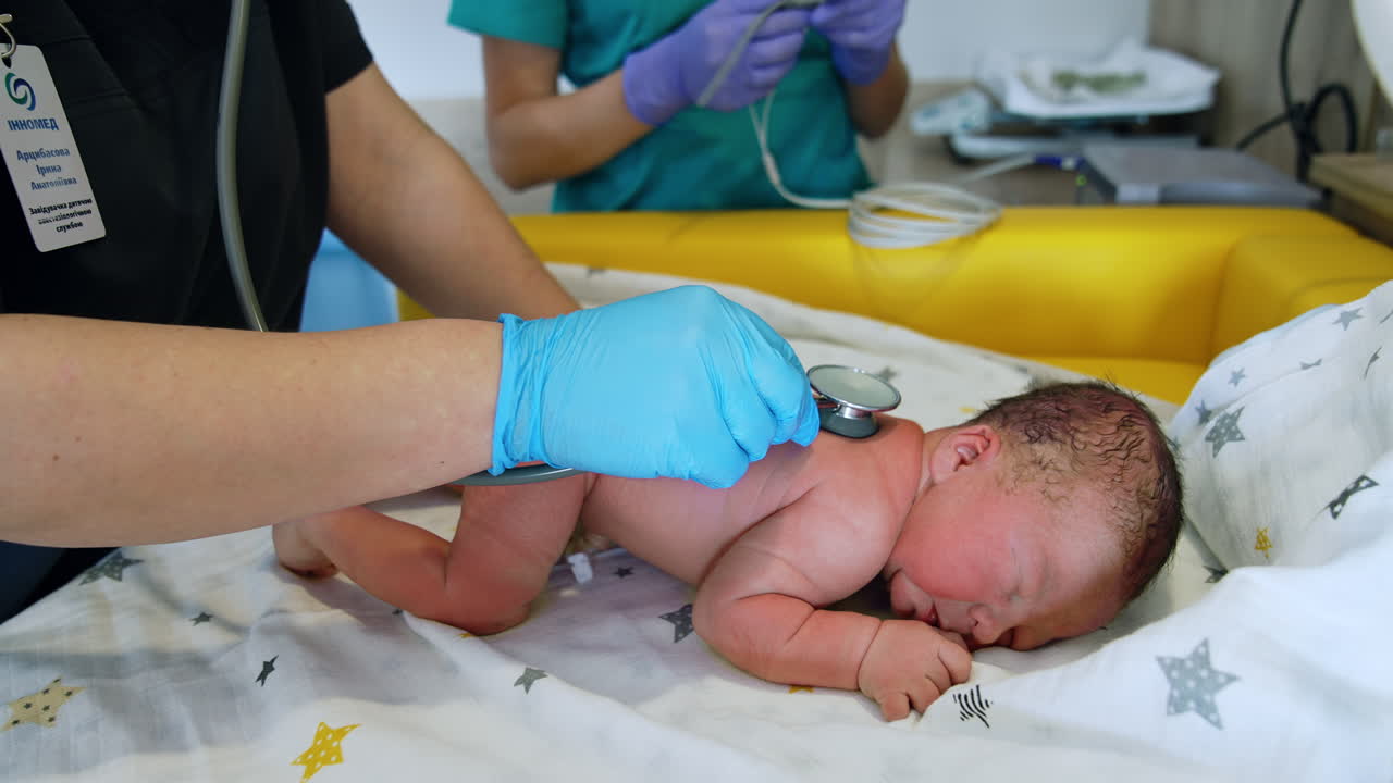 Adorable newborn naked baby lies on the belly. Neonatologist listens to child's heart with stethoscope.