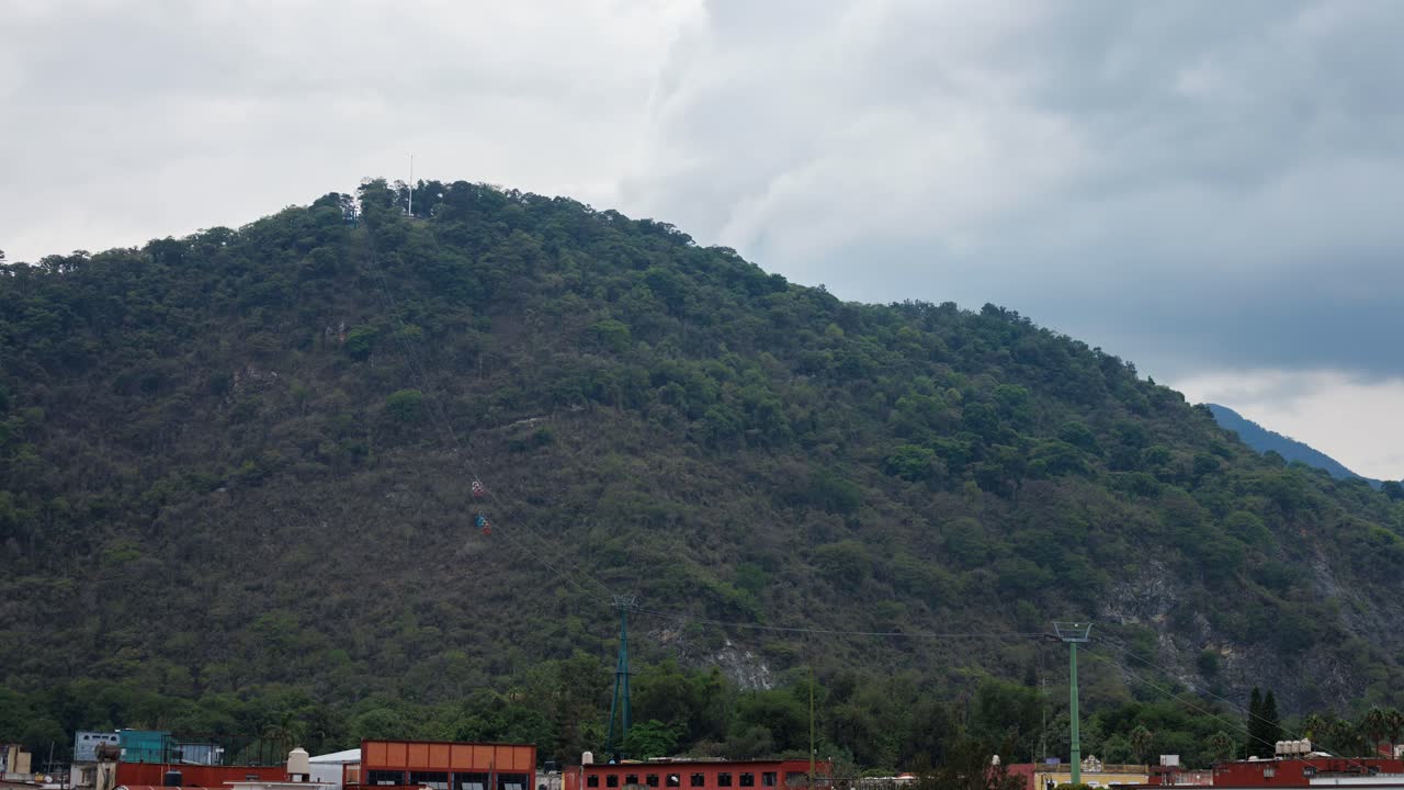 Timelapse do Cerro del Borrego enquanto cabines de teleférico deslizam pela encosta sob um céu nublado, com nuvens se movendo rapidamente e luz suave mudando sobre a montanha em Orizaba