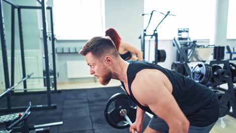 athletic woman and man in sportswear lifting barbell in the gym. persistent couple doing hard workout with heavy equipment standing in front of the mirror in modern sports club.