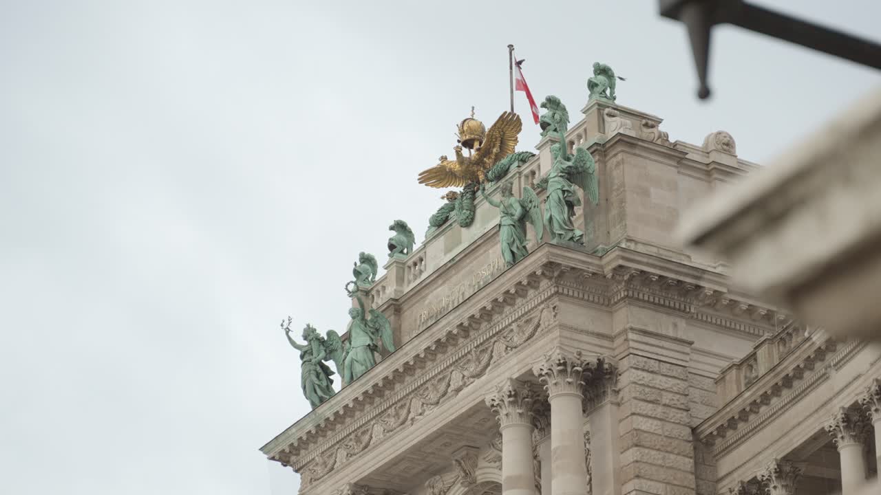 de cerca en el impresionante palacio imperial de hofburg en viena austria con sus esculturas y el águila en la parte superior mientras la bandera austriaca está ondeando en el viento y los pájaros volando alrededor en un día nublado