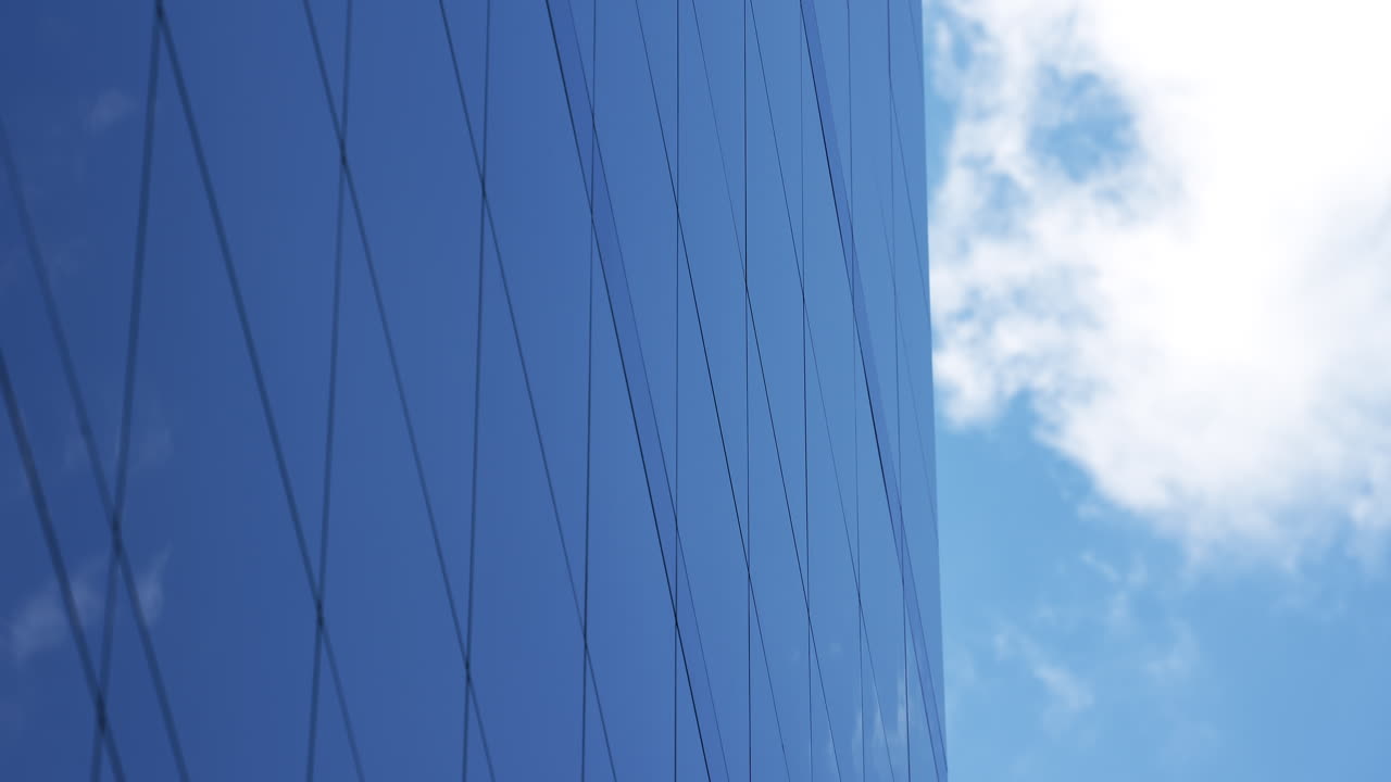Veduta dal basso della facciata di un moderno edificio in vetro contro un cielo blu.