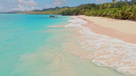 low altitude drone flight showing waves of caribbean sea arriving sandy beach during sunny day - aerial establishing forward shot