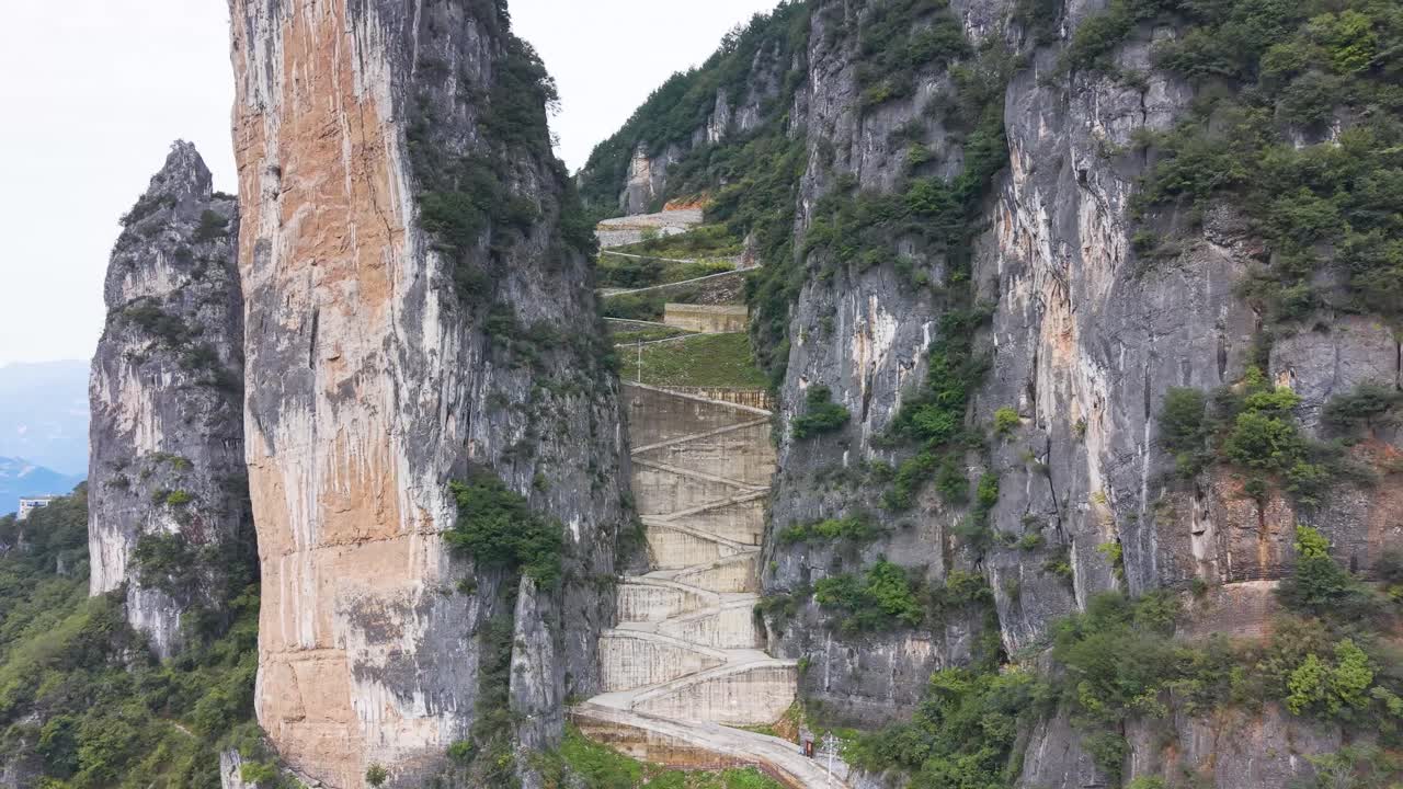 Top-down aerial view of the steep, sheer rock formations and the zigzag road carved into the cliffside at Lingpaishi, Wuxi County, China. Captures remote natural beauty and engineering. UHD