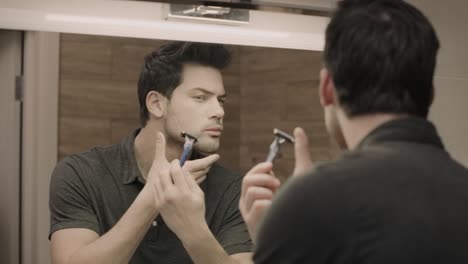 Young-man-shaving-face-in-front-of-mirror-at-bathroom.-Portrait-of-handsome-guy