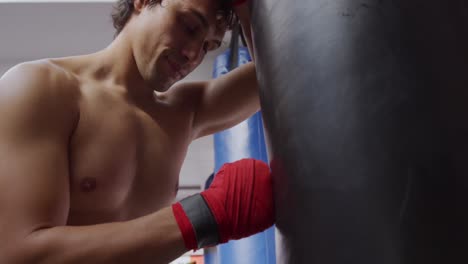 Caucasian-man-resting-on-punchbag-in-boxing-gym