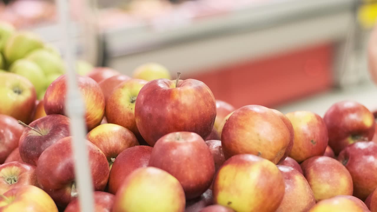 고무 장갑을 입은 여성이 신선한 사과를 뽑아 슈퍼마켓에서 플라스틱 봉투에 넣습니다.