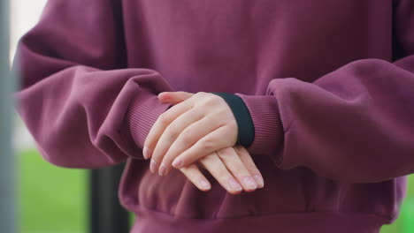 confident participant hoodie performs gentle hand stretch by pressing palms together and flexing fingers during calm relaxation phase before outdoor workout under open sky at urban fitness park