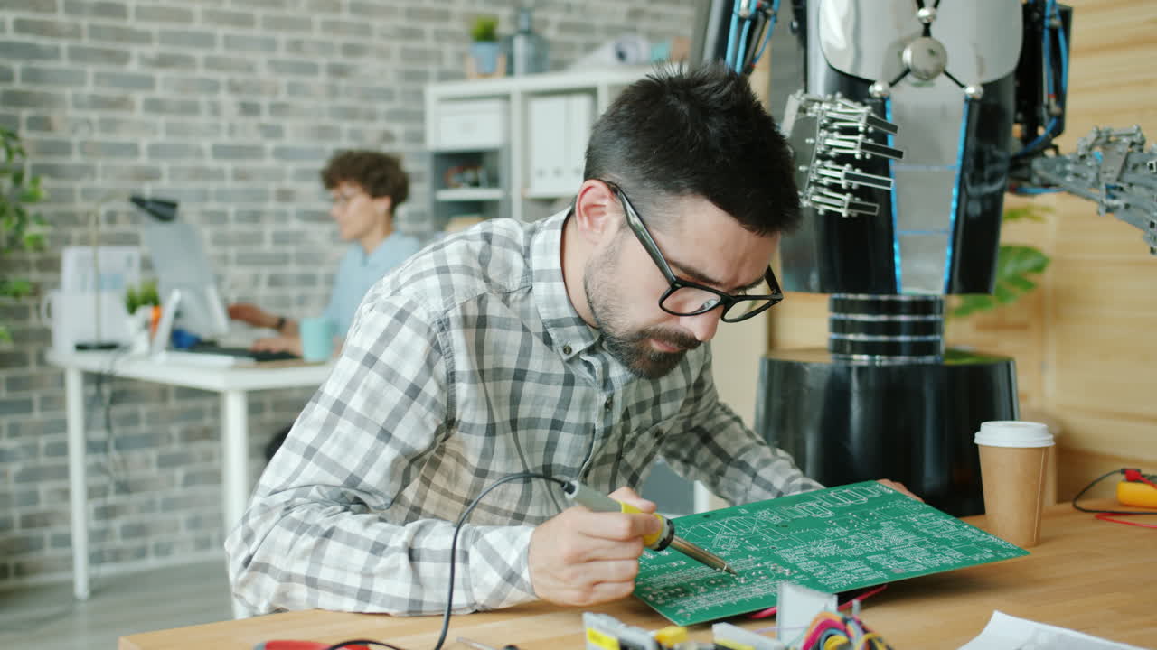 Engineer Soldering Circuit Board with Robot in Background