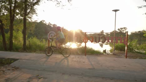 una toma panorámica estacionaria de una mujer que viaja en bicicleta con alforjas pasando por un parque público en la orilla del río en isan, tailandia