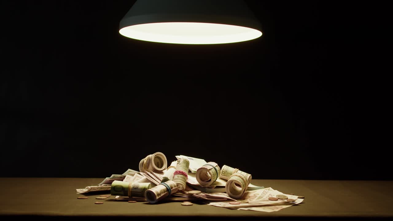 Pile of Cash and Coins Illuminated by a Lamp in a Dark Room