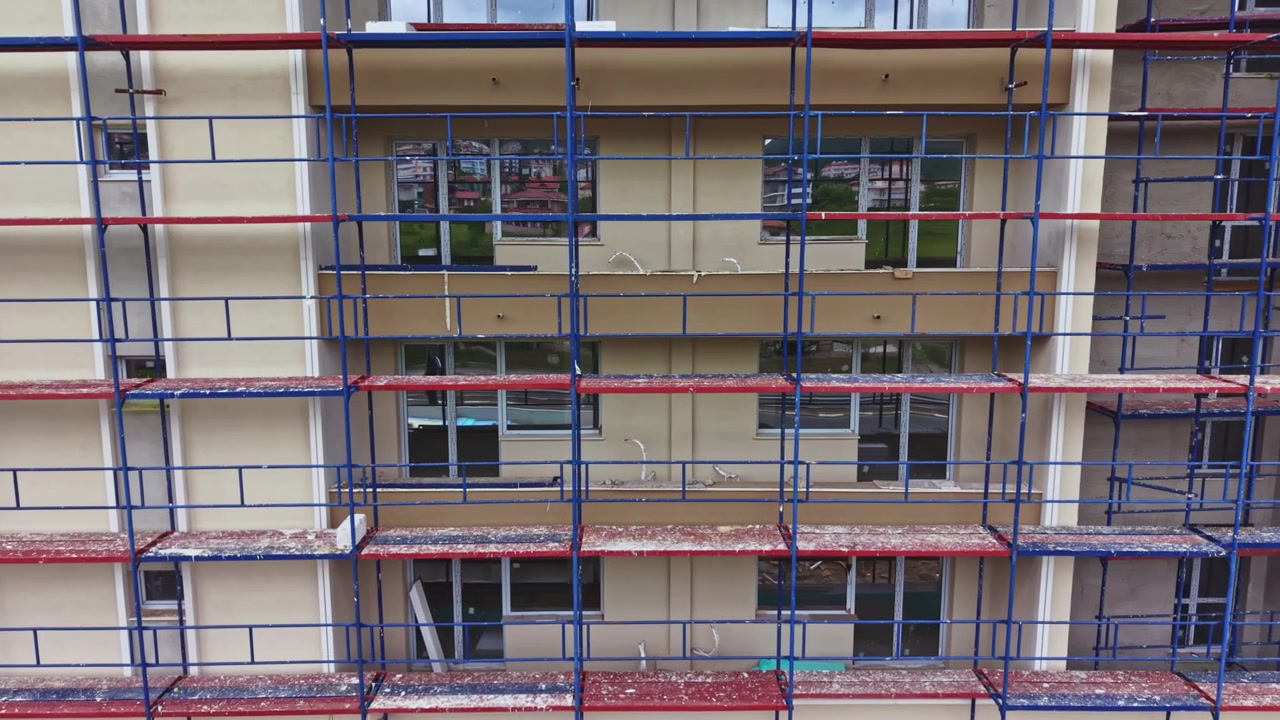 Fleretagers stillads omgiver beboelsesejendom under vedligeholdelsesarbejde. Luftdrone fanger igangværende renovering med sikkerhedsforanstaltninger og udstyr på plads