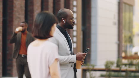 Hombre-De-Negocios-Afroamericano-De-Pie-Con-Teléfono-Inteligente-Y-Café-En-La-Calle