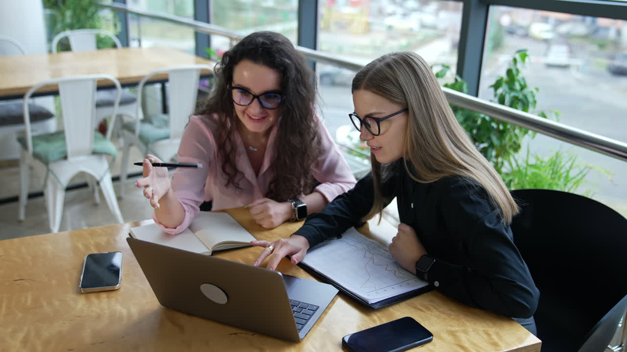 Business discussion between two colleagues sitting at the table in front of laptop. Comfortable working place in a large office.