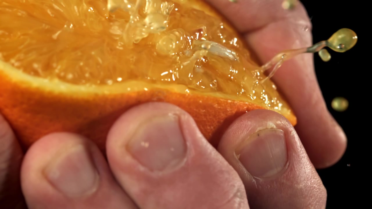 Nærbillede af hånd der presser frisk appelsin med sprøjtende saft
