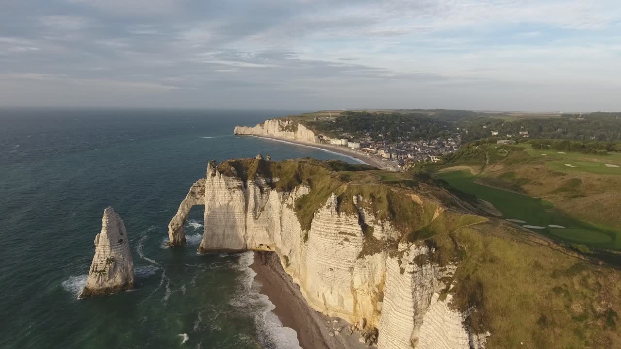 volando sobre el arco natural de etretat con la ciudad y la bahía en el fondo.