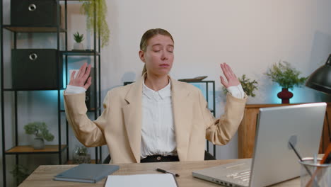 Businesswoman-working-on-laptop-meditating-doing-yoga-breathing-exercise-in-lotus-position-at-office