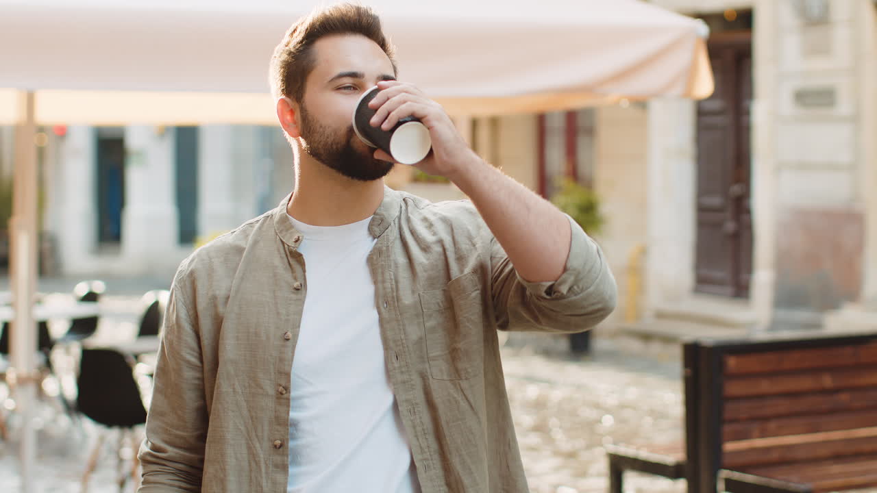 Young man guy enjoying drinking morning coffee hot drink relaxing taking a break in city street