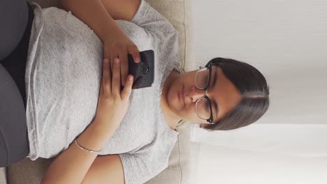 Brunette-pregnant-woman-with-glasses-sitting-typing-on-a-mobile-phone