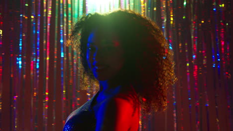 portrait of young woman having fun in nightclub or bar dancing against sparkling tinsel curtain in background