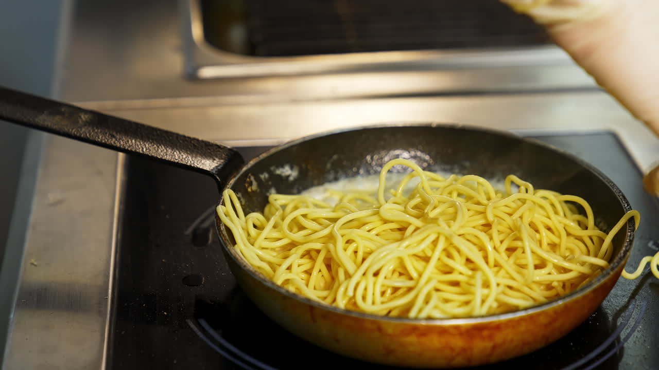 Man in white gloves puts spaghetti on a pan with white sauce. Bechamel in frying pan with pasta. Delicious dish video.