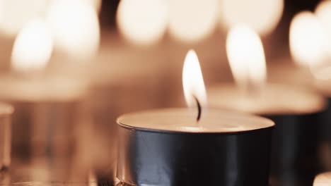 video of rows of tea candles with white flames and copy space on black background