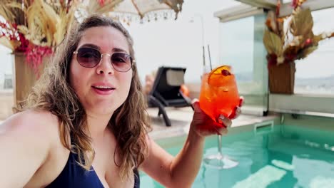 a stylish young woman enjoying a drink at a luxury rooftop pool on a sunny day