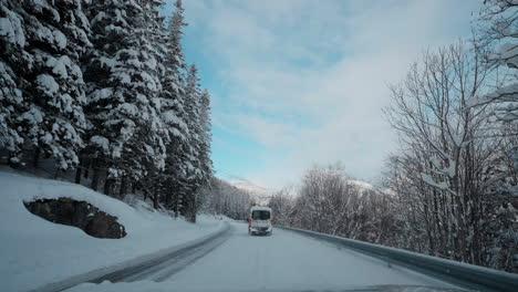 POV-video-of-a-daytime-drive-through-the-snowy-roads-of-Norway's-Western-Fjords,-surrounded-by-tall,-snow-covered-mountains-with-trees