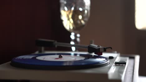 starting playback of vintage blue vinyl record with glass of white wine in background